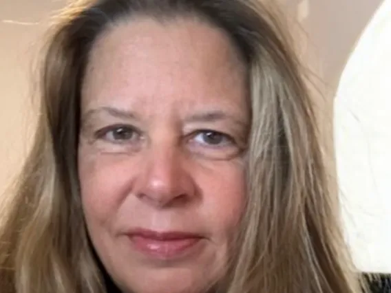 Christine smiles and stands in front of a beige background in this close up image.