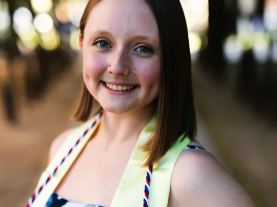 Megan poses in graduation regalia. She stands in front of a blurred cityscape.