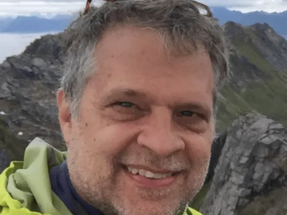 Scott takes a photo during fieldwork. He wears a yellow rain jacket and stands on a hill.