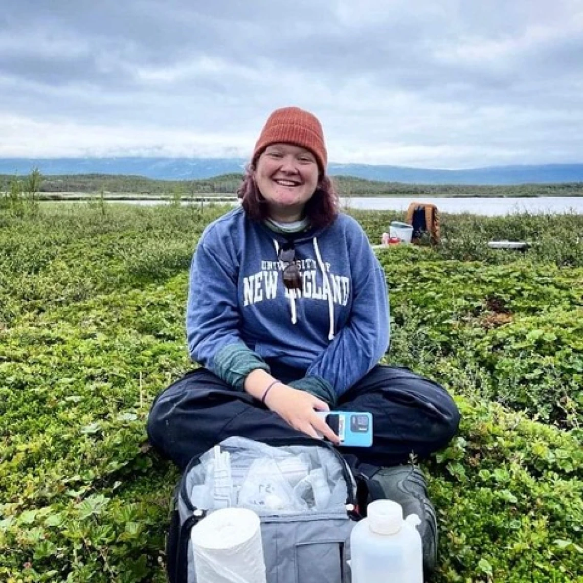 Jes sits in a field of green in Arctic Sweden with her collection kit on the ground in front of her. 