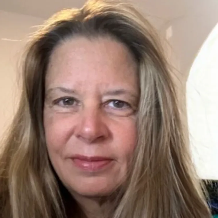 Christine smiles and stands in front of a beige background in this close up image.