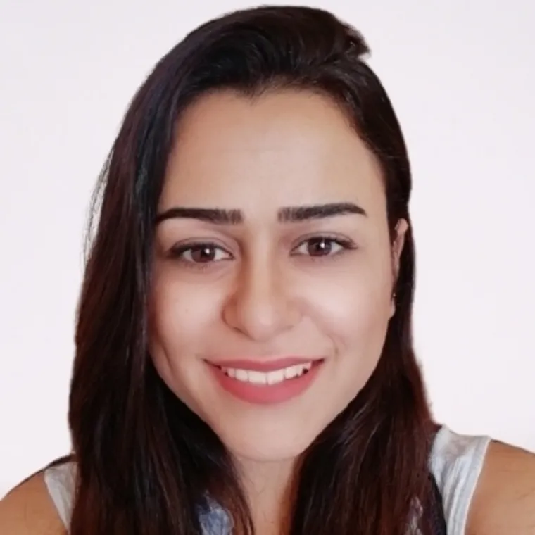 Ghiwa stands in front of a plain, light background. She wears a white sleeveless top and smiles warmly. 