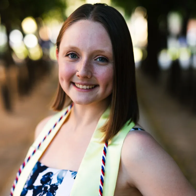 Megan poses in graduation regalia. She stands in front of a blurred cityscape.